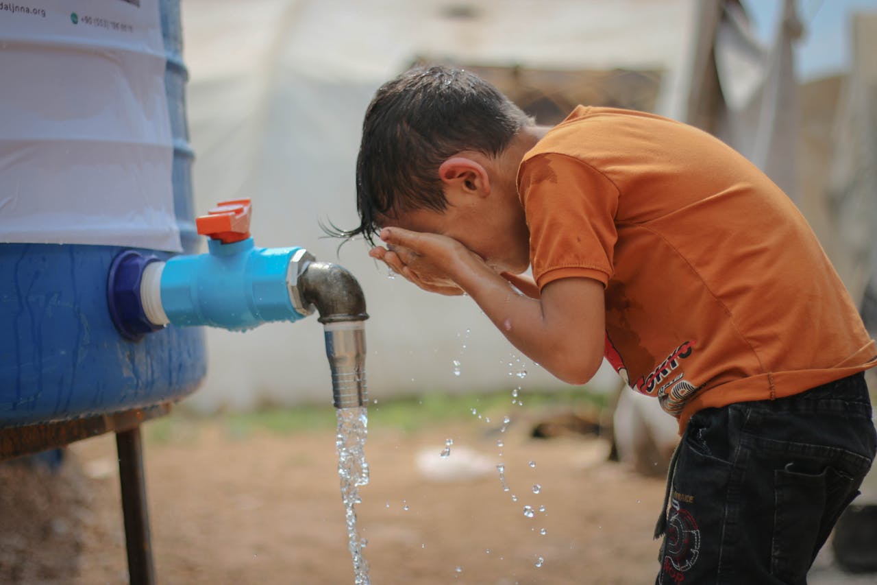 A young boy cools off by splashing water from an outdoor faucet on a hot summer day in Idlib, Syria.