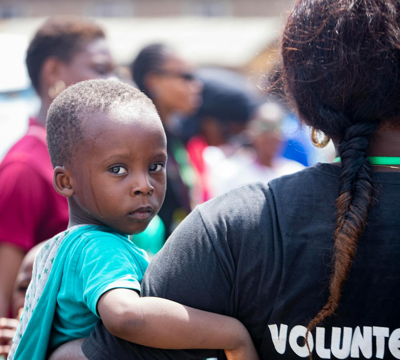 A child held by a volunteer during a community event outdoors, showcasing care.